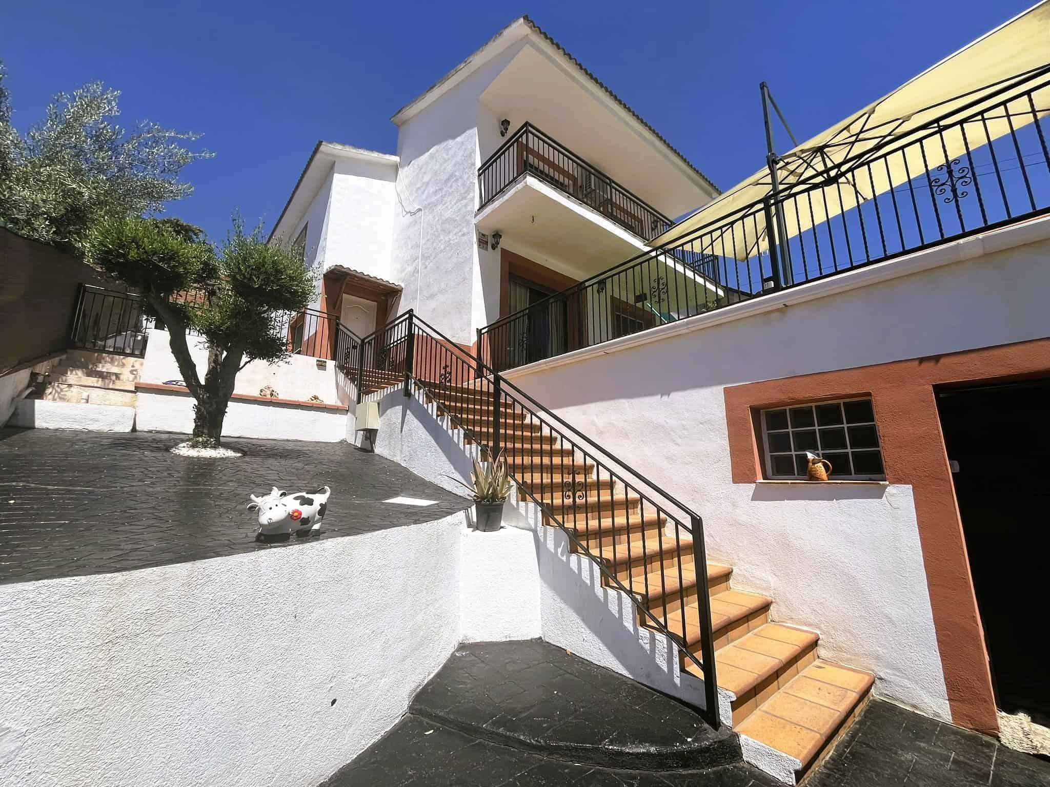 Escala exterior d'una casa blanca amb terrasses, baranes de ferro negre i escales de rajola terracota sota un cel Blau, enfocada a serveis immobiliaris i advocats especialitzats en serveis immobiliaris.