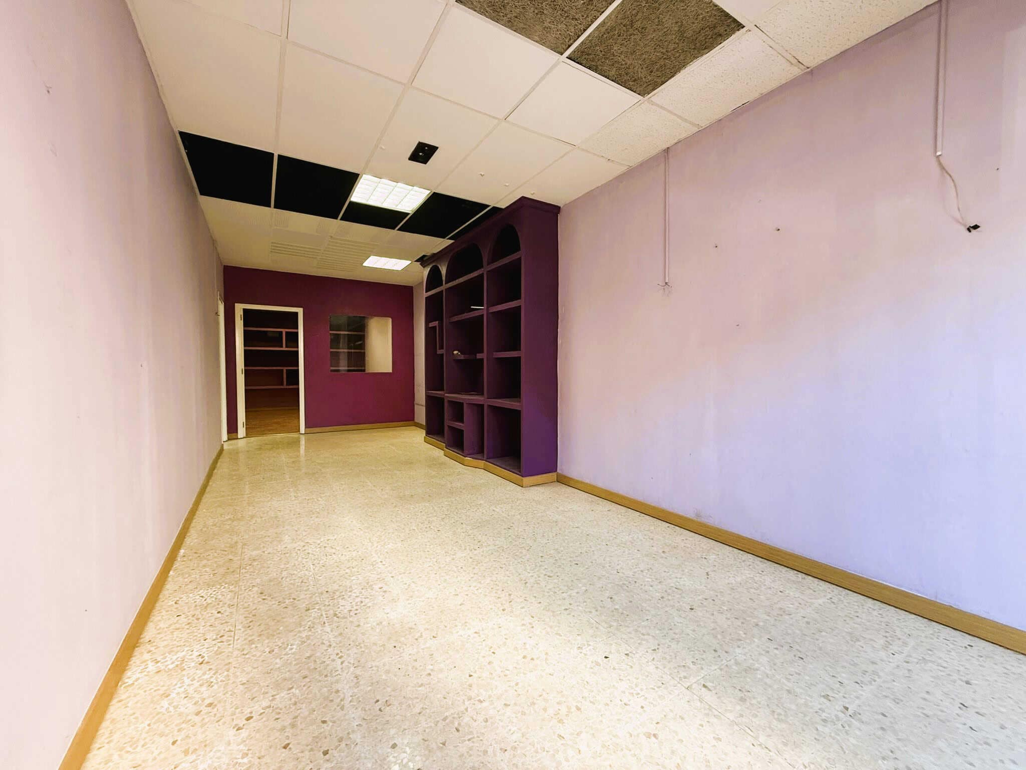 Espai immobiliari buit amb parets en roig, làmpades i prestatgeries, ideal per a activitats relacionades amb serveis immobiliaris i assessoria legal en el sector immobiliari.