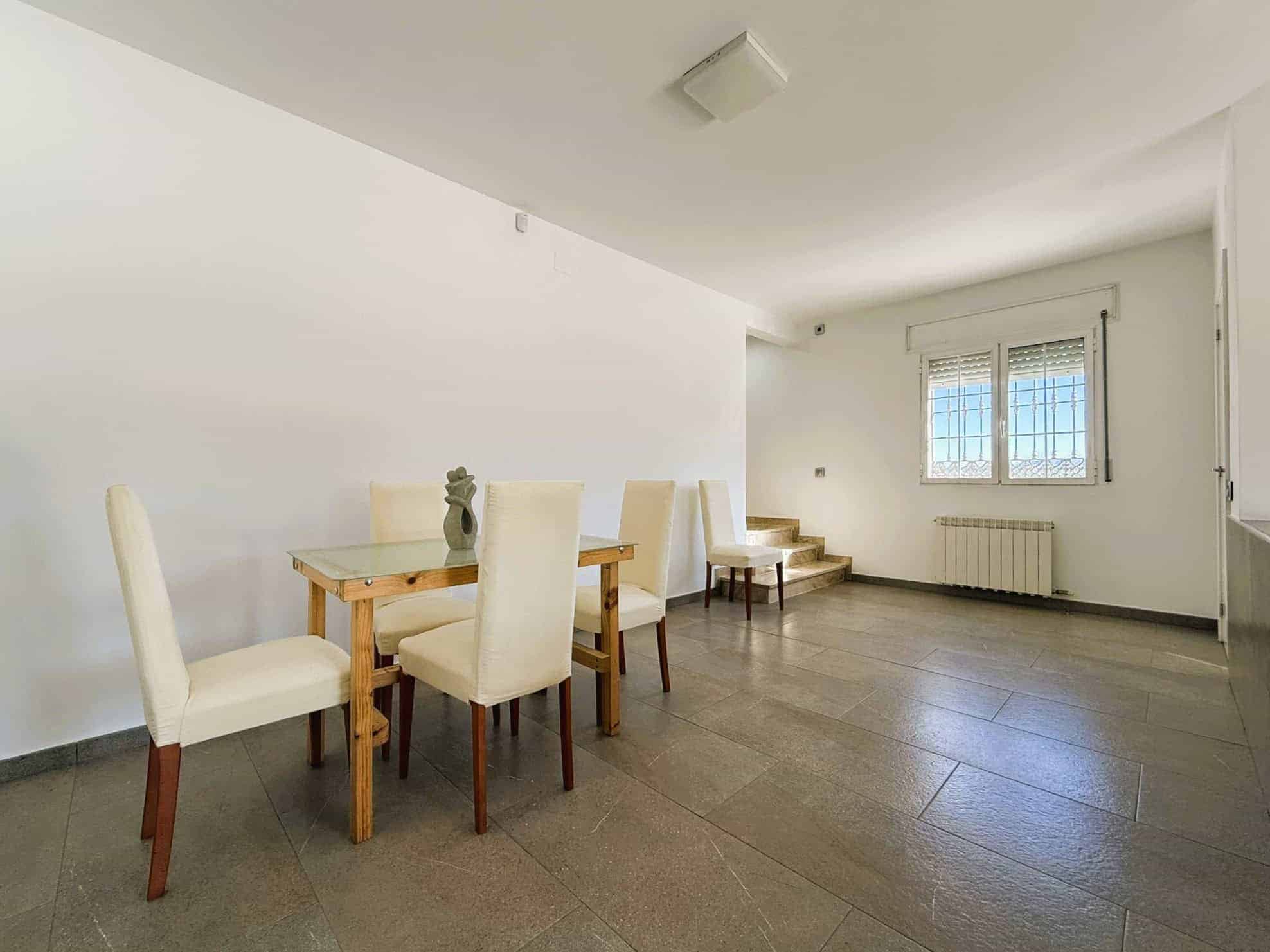 Sala d'estar amb llar de menjador, lluminosa i espaiosa, amb grans finestrals, decoració moderna i mobiliari blanc, ideal per a habitatge o inversió immobiliària.