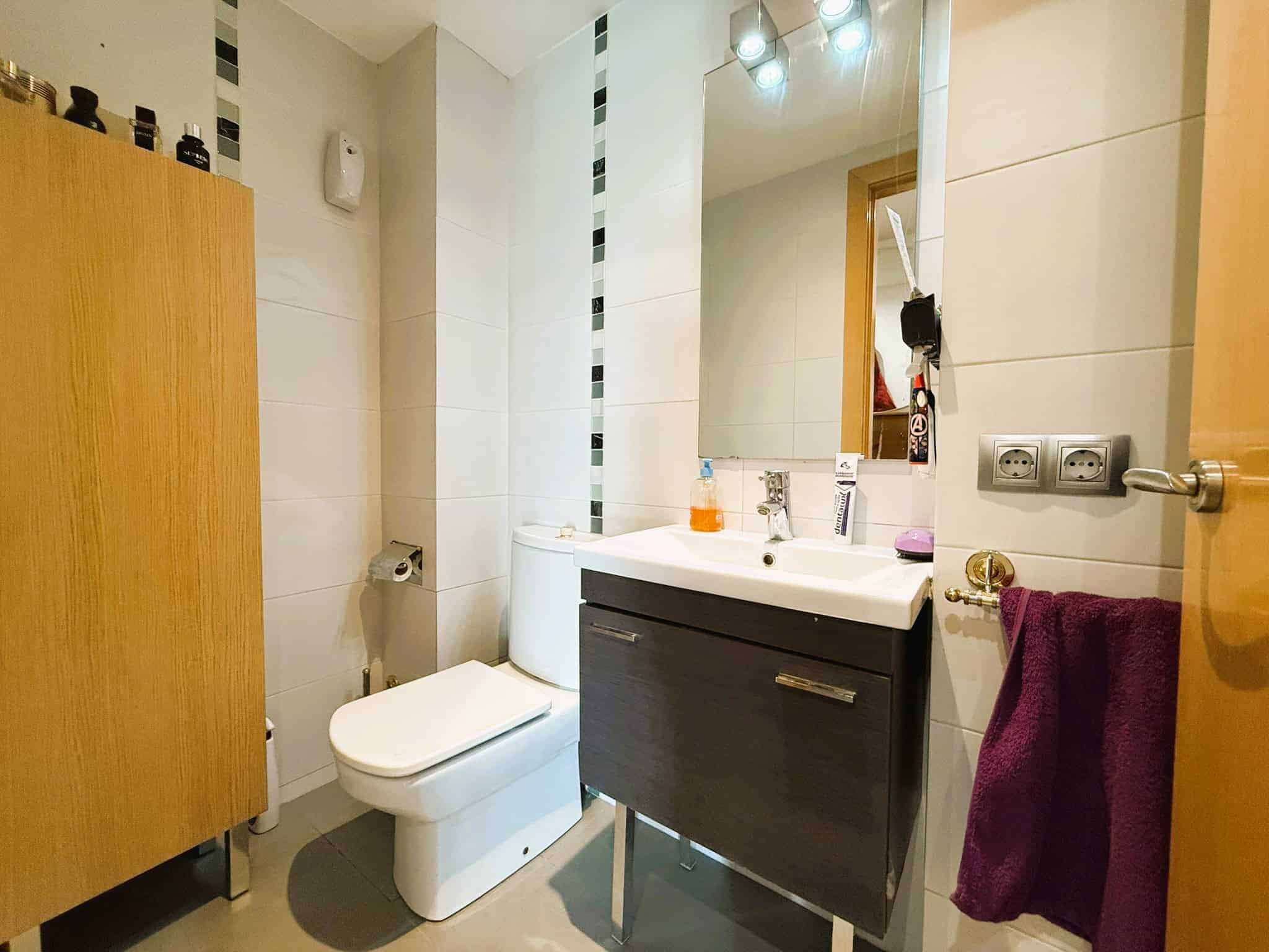 Fa mésores de bany modern amb lavabo, mirall, tovalloller i accessoris a la paret. Decoració funcional, superfície de plaques de porcelana, ambient lluminós i pràctic per a habitatges o oficines.