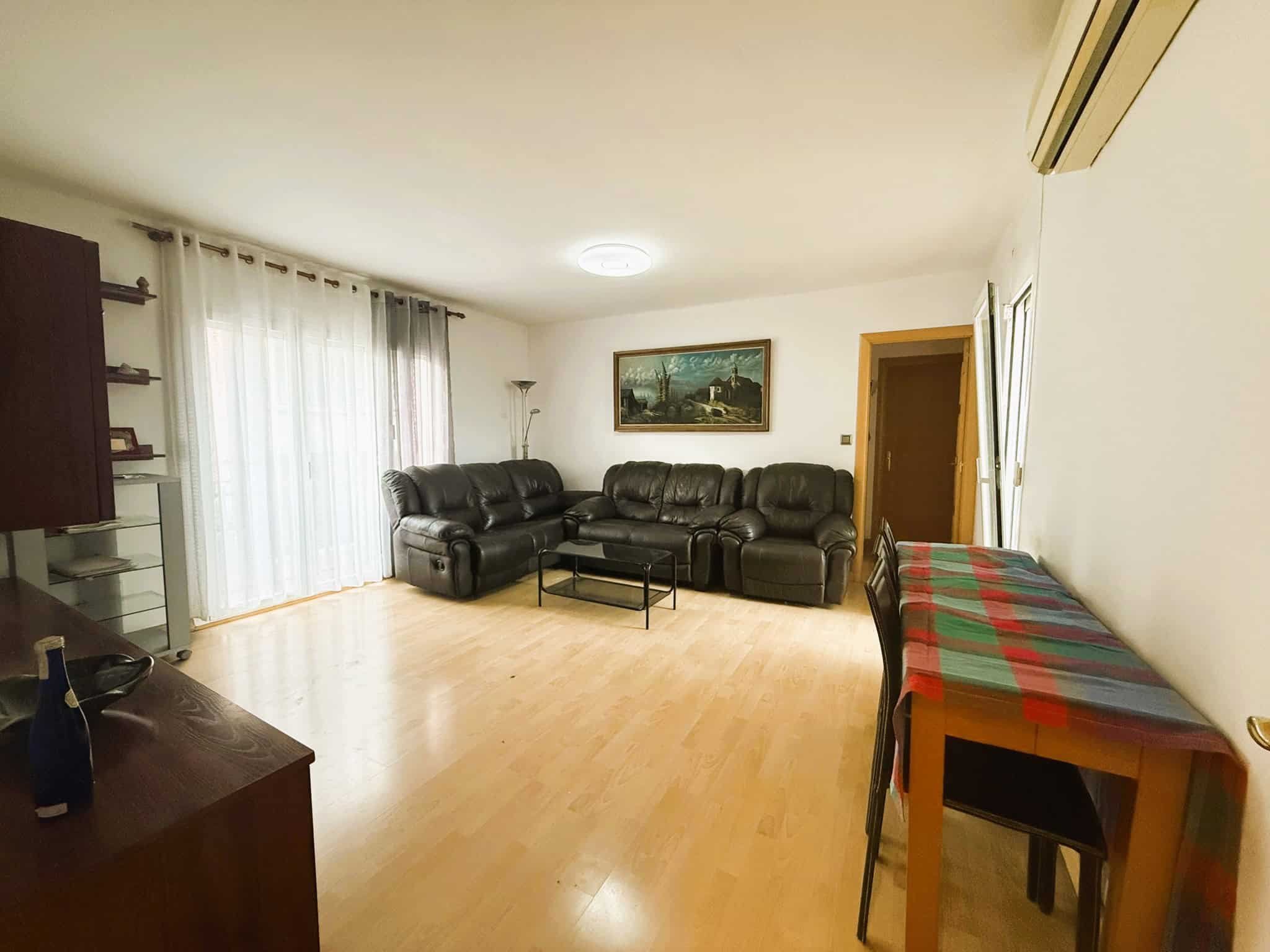Imatge de saló modern amb sofàs de cuir negre, finestra amb cortines de cortina blanca, decoració minimalista i espai.llarg. Ideal per a serveis immobiliaris i assessorament legal en immobles.