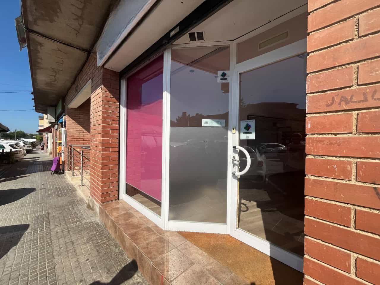 Lloc comercial en venda amb finestra de vidre i porta d'accés a la botiga, ubicat a peu de carrer amb espai per a clientela i aparcament proper.
