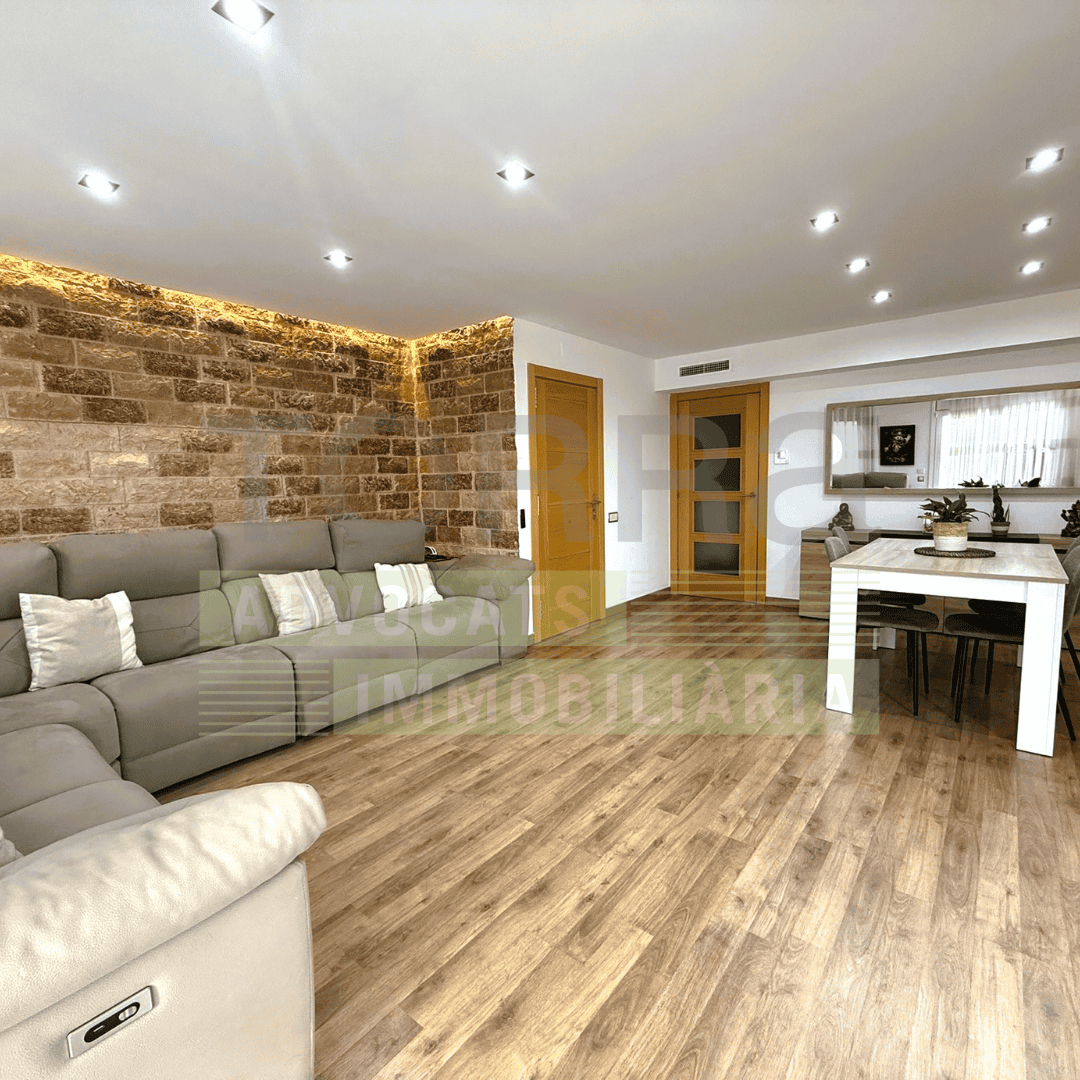 Imatge d’un pis modern amb espaiosa sala d’estar que combina estils rústic i contemporani, amb parets de pedra, sòls de fusta, il·luminació Led i mobles acollidors, ideal per a compradors interessats en serveis immobiliaris i advocats especialitzats.