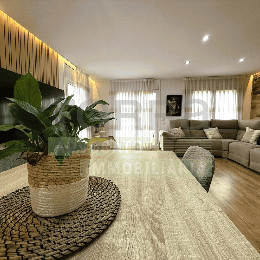 Text alternatiu: Sala d'estar moderna amb gran sofà, elements decoratius, i gran finestra amb cortines lleugeres, ideal per a habitatges de qualitat.