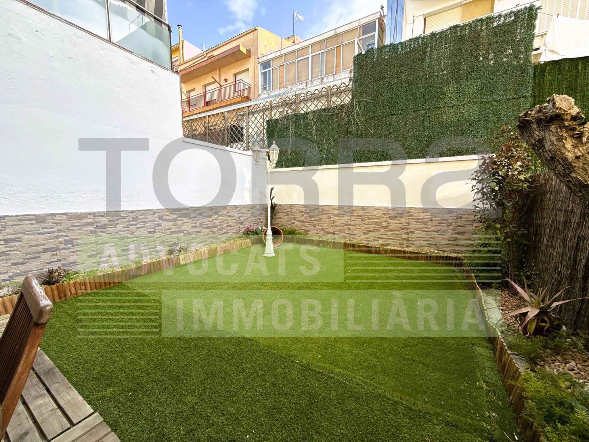 Imatge d'una tanca de jardí amb gespa artificial, ideal per a espais residencials i immobiliaris, amb zona de descans i decoració exterior.