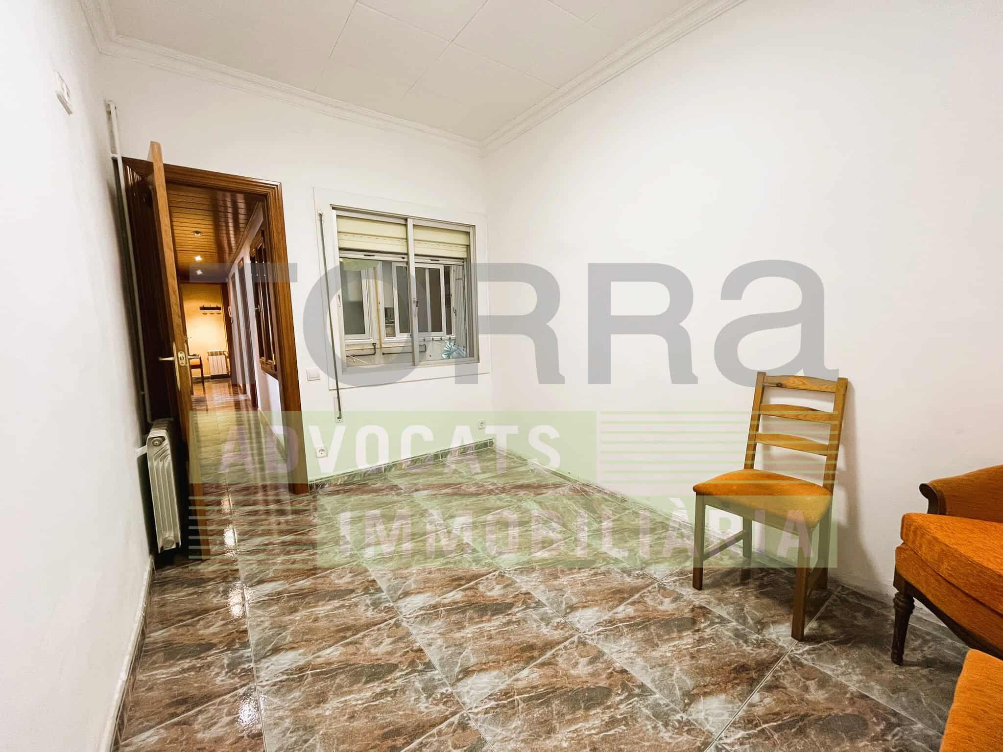 Sala d'espera o oficina amb mobiliari senzill, finestra i terres de rajola, ideal per a serveis immobiliaris o advocats.