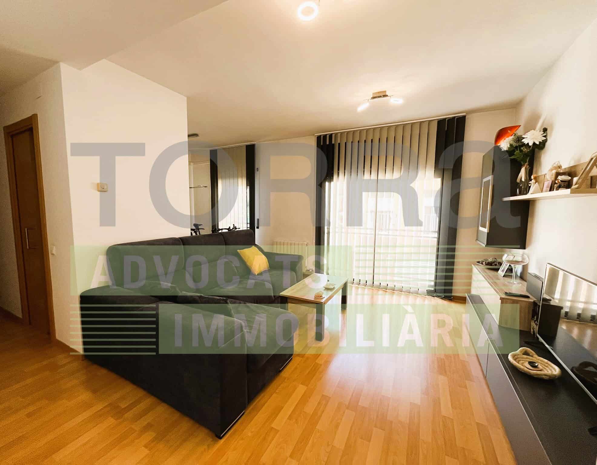 Sala d'estar acollidora amb sofà verd, televisió i balcó amb cortines, decorada amb elements moderns i llum natural abundant.